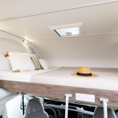 Interior view of a truck sleeper cab with a raised bed, cushions, and a straw hat on the mattress.